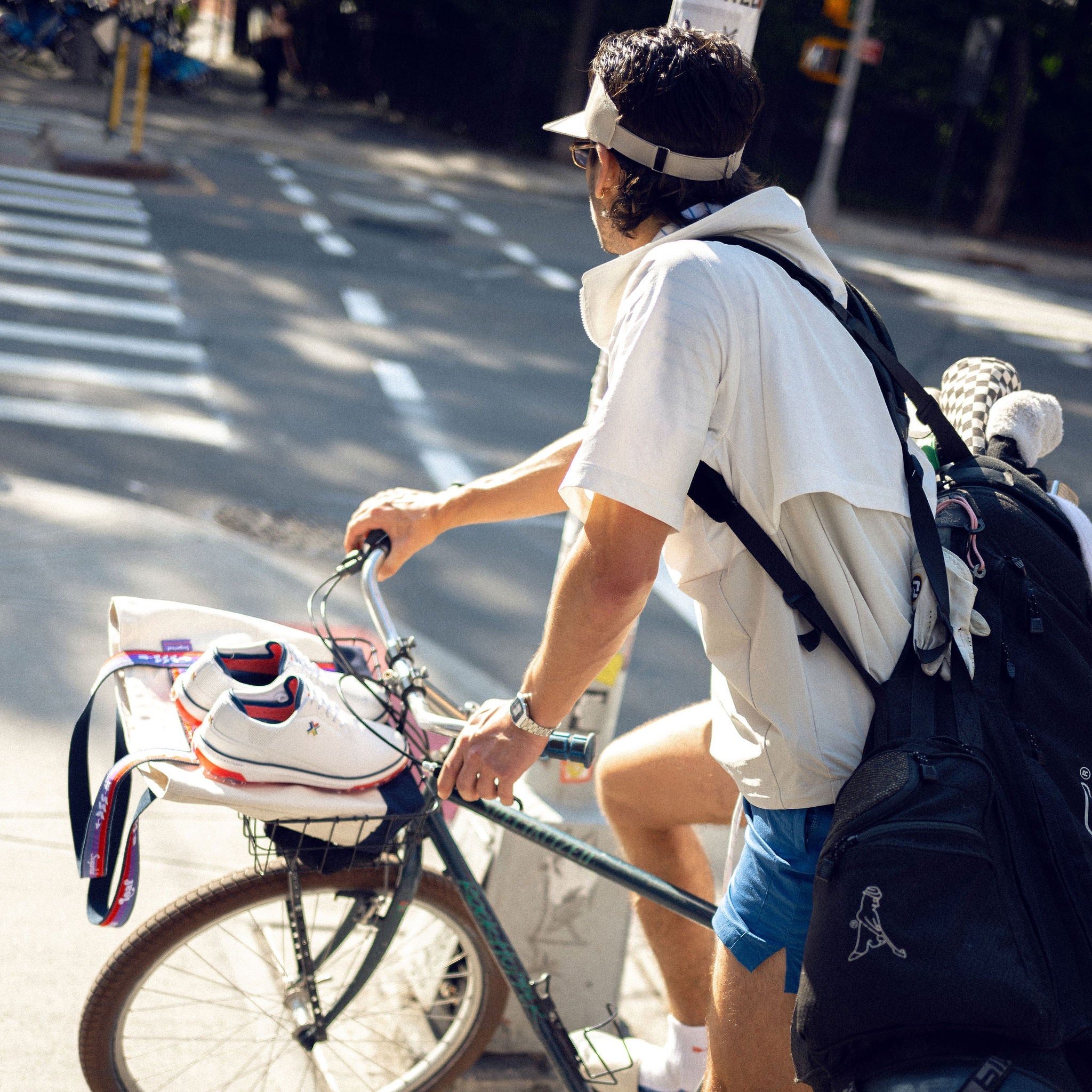 Person riding a bicycle on a city street with a backpack and visor and golf bag