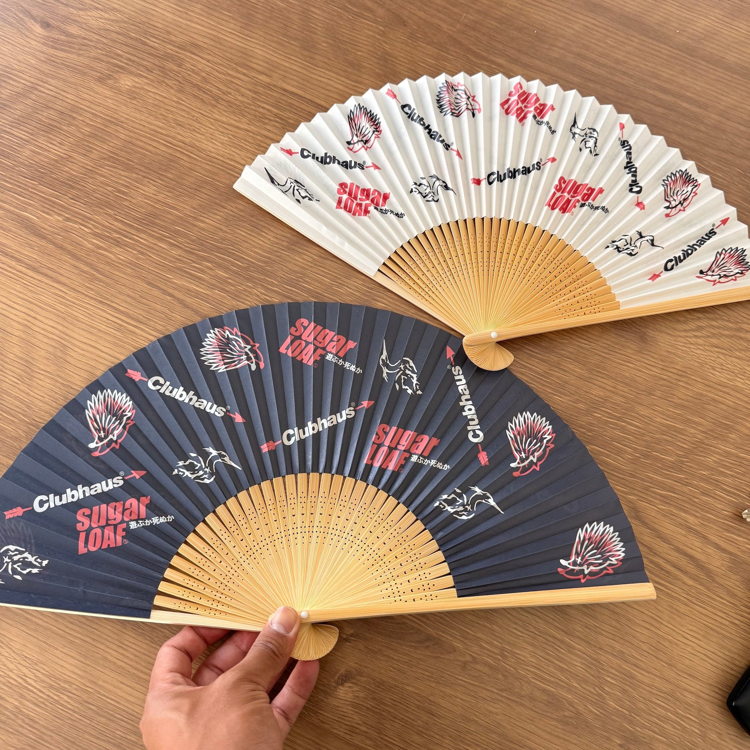 Two fans, one blue and one white with branding, on a wooden surface.