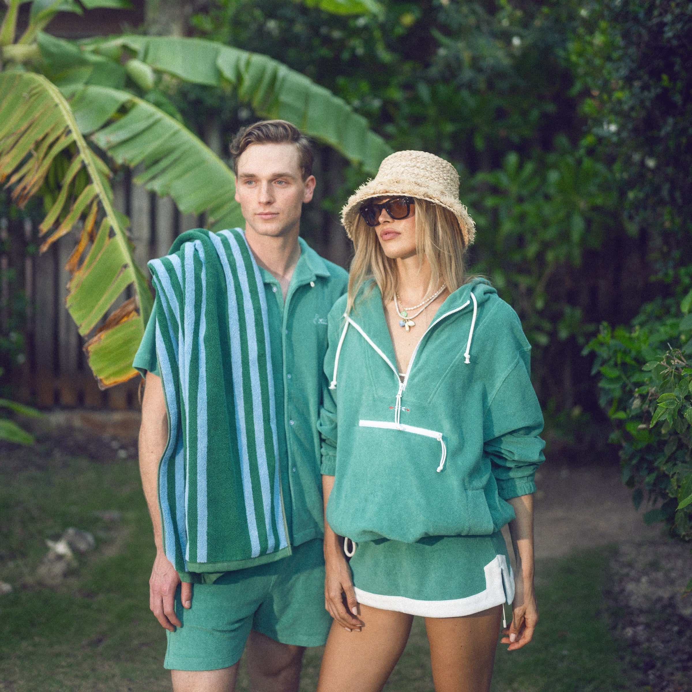 Two people in green outfits standing in a lush, green outdoor setting.