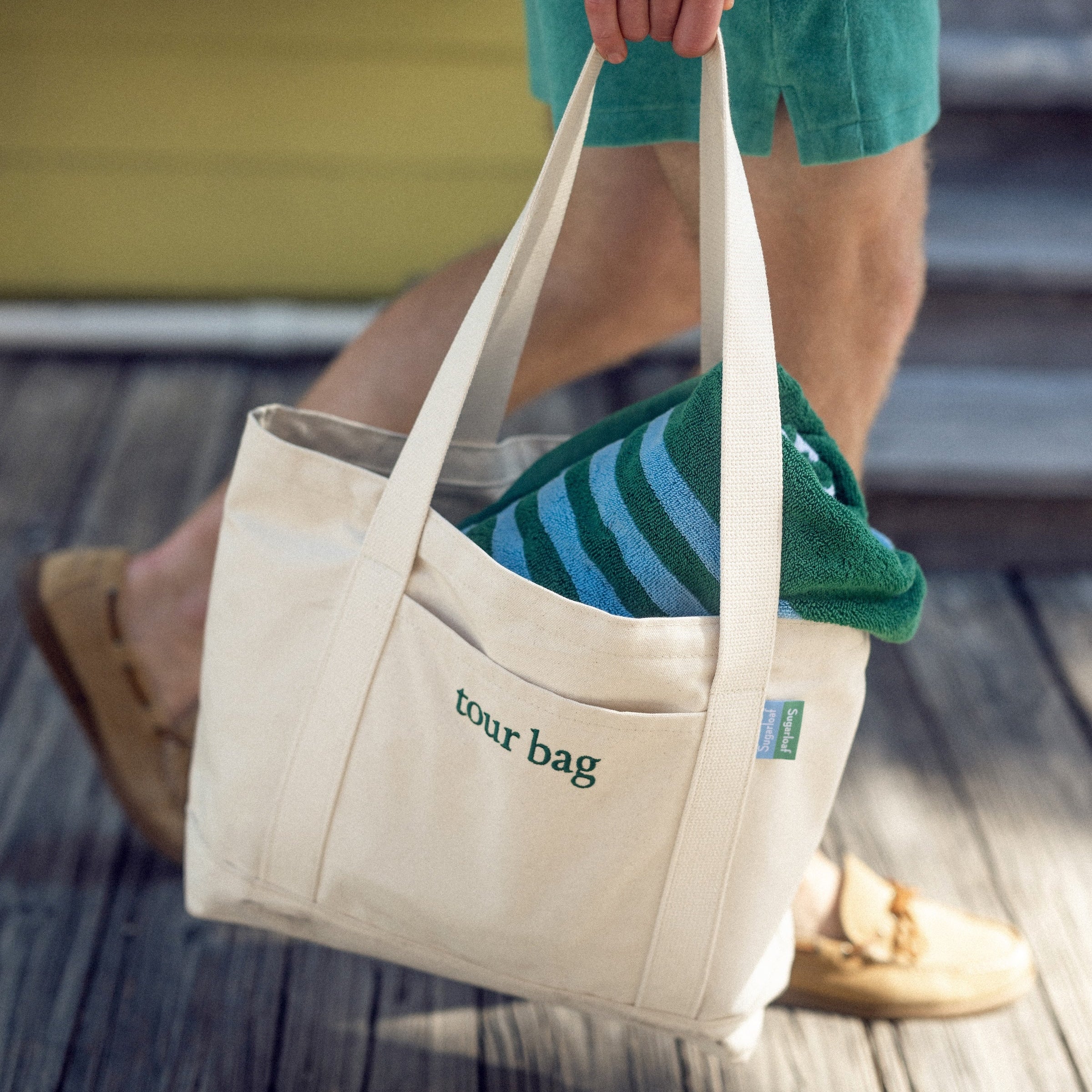 Person holding a beige tote bag with 'your bag' text on a wooden floor.