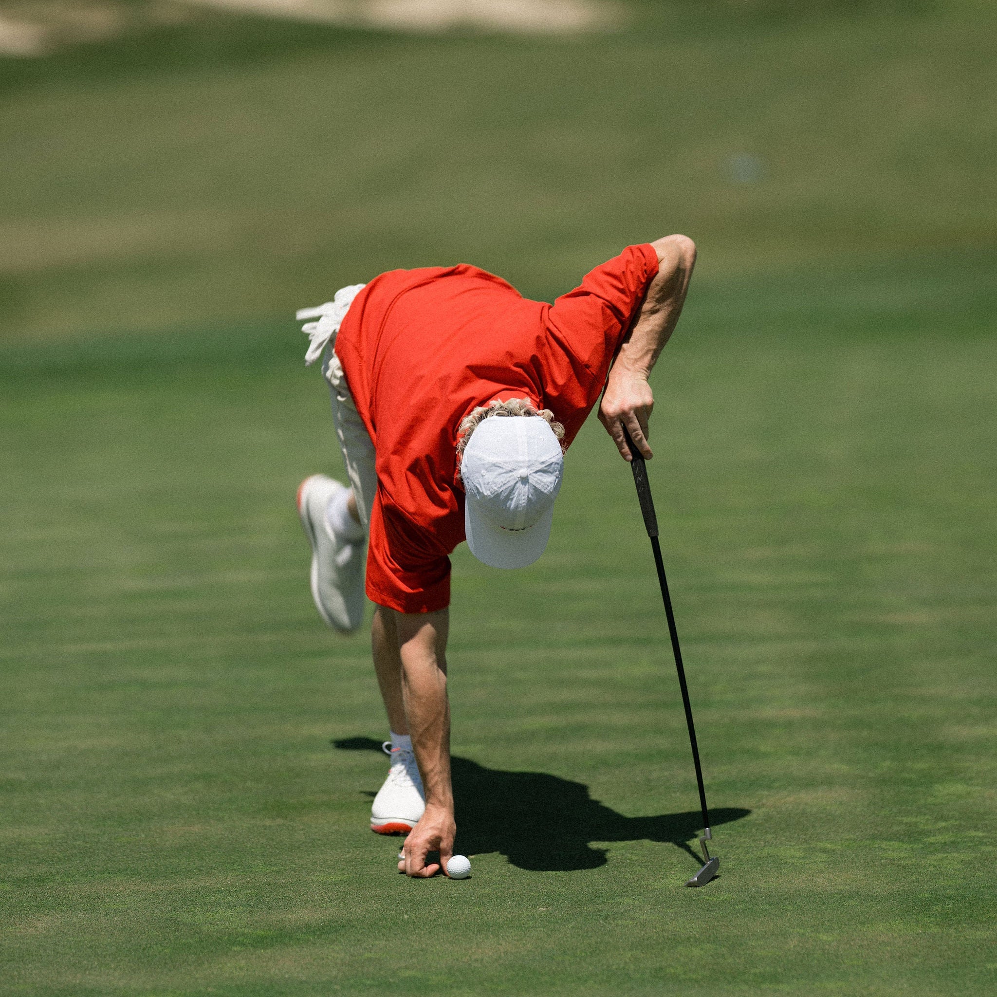 Person in red shirt and white cap playing golf on a green course